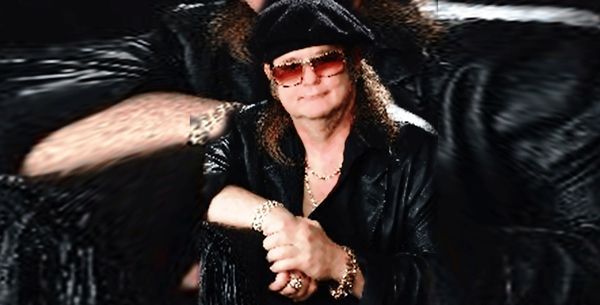 Man in black leather outfit, sunglasses, beret; posing with arms crossed.