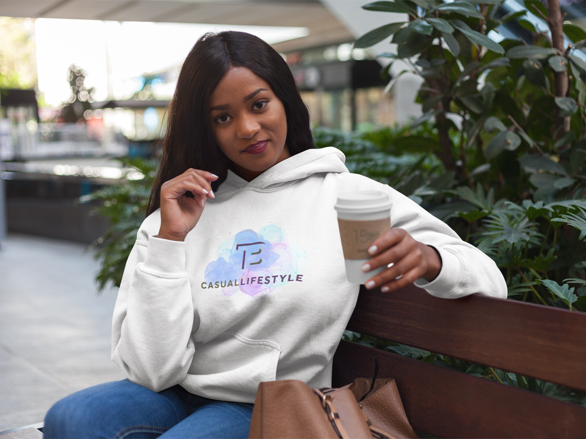 Woman in white hoodie with coffee, sitting on bench outdoors.