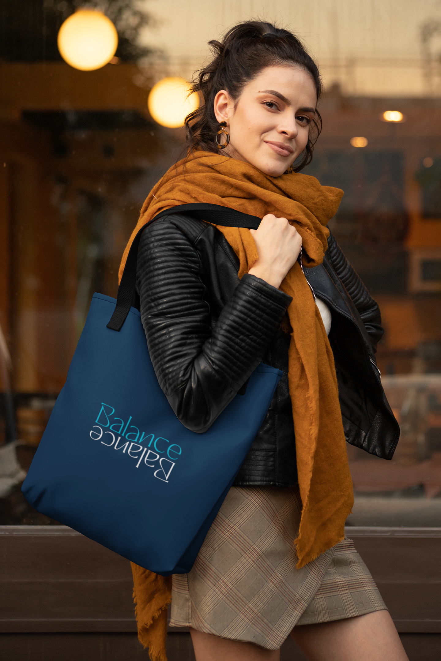 Woman in jacket and scarf, carrying blue tote bag with text outside a building.