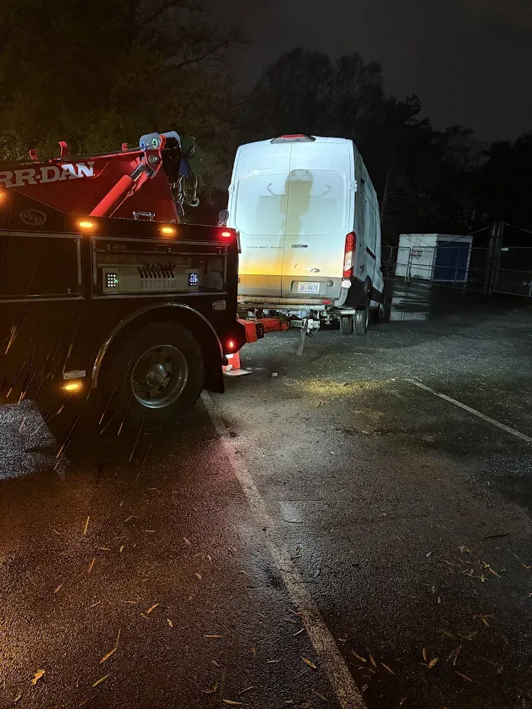 Tow truck at night towing a white van, parked on asphalt.