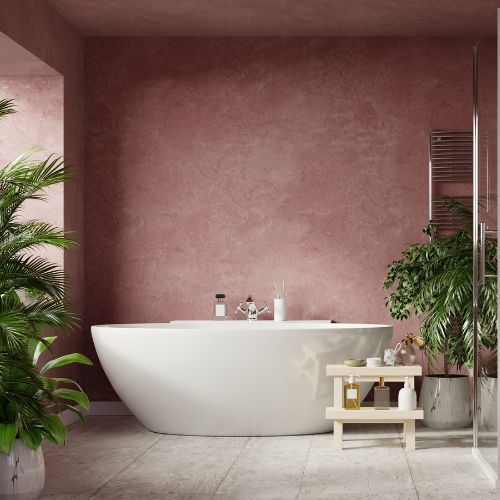 A larger white soaker tub in a bathroom with light red walls surrounded by plants.