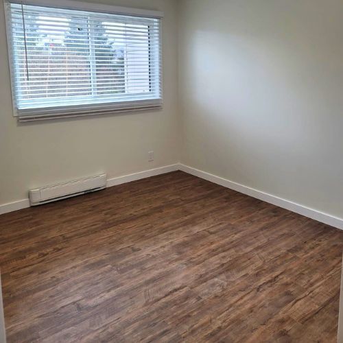 Brown laminate flooring in a bedroom with white baseboards and grey walls.