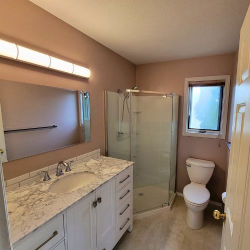 A modern bathroom renovation with a new vanity, counter, bar light, and a corner shower.