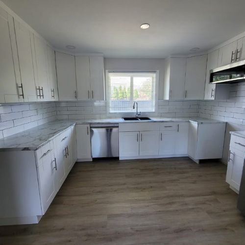 A modern white kitchen with gold finishings, marble countertop, and laminate flooring.