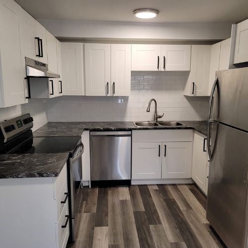 A kitchen with white cabinets, stainless steel appliances, and dark brown laminate flooring.