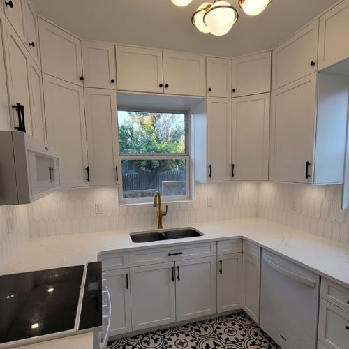 A white modern kitchen with black finishes, and a golden faucet on the sink.