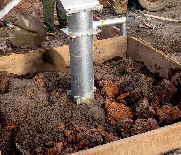 Worker pouring concrete around a metal post in a wooden form outdoors