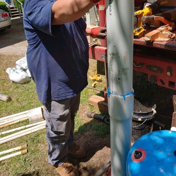 Worker beside a red truck operating a tall white metal pole outdoors.