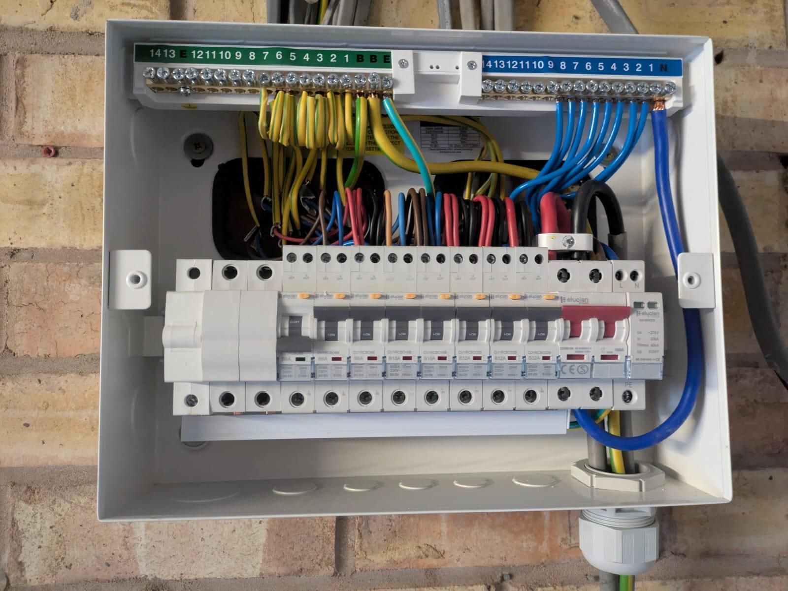 Electrical distribution box with wires of various colors, mounted on a brick wall.