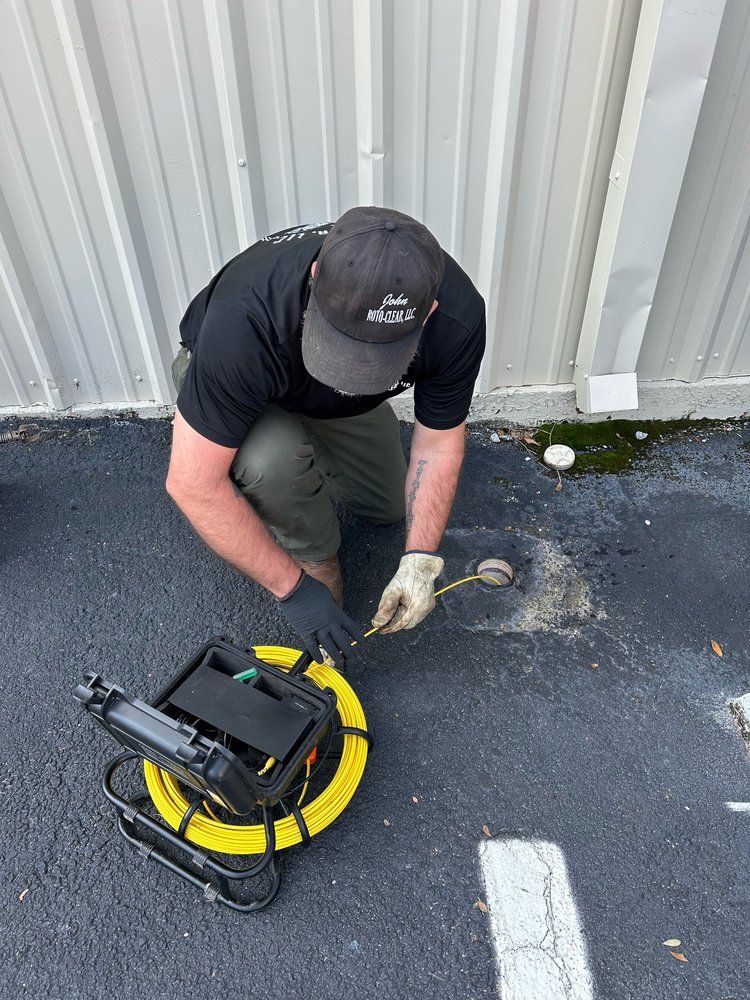 Man in black shirt and cap using a cable locator on asphalt next to a building.