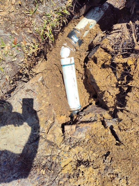 White PVC pipe with elbow fitting in a dirt trench, partially exposed.