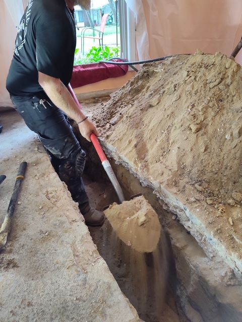 Person shoveling dirt from a trench inside a building with a large pile of dirt next to them.