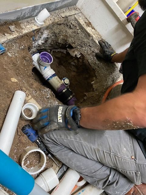 Plumber in a bathroom repairing a pipe. He is kneeling, working inside a hole in the floor.