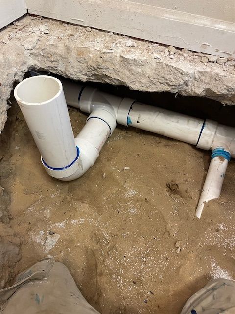 White PVC drain pipes installed in a floor opening.