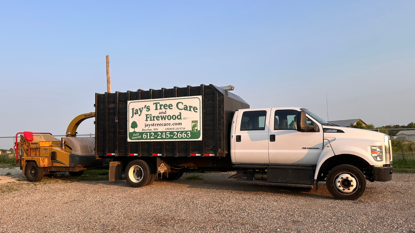 White truck with Joe's Tree Care logo hauling a wood chipper trailer on a gravel road.