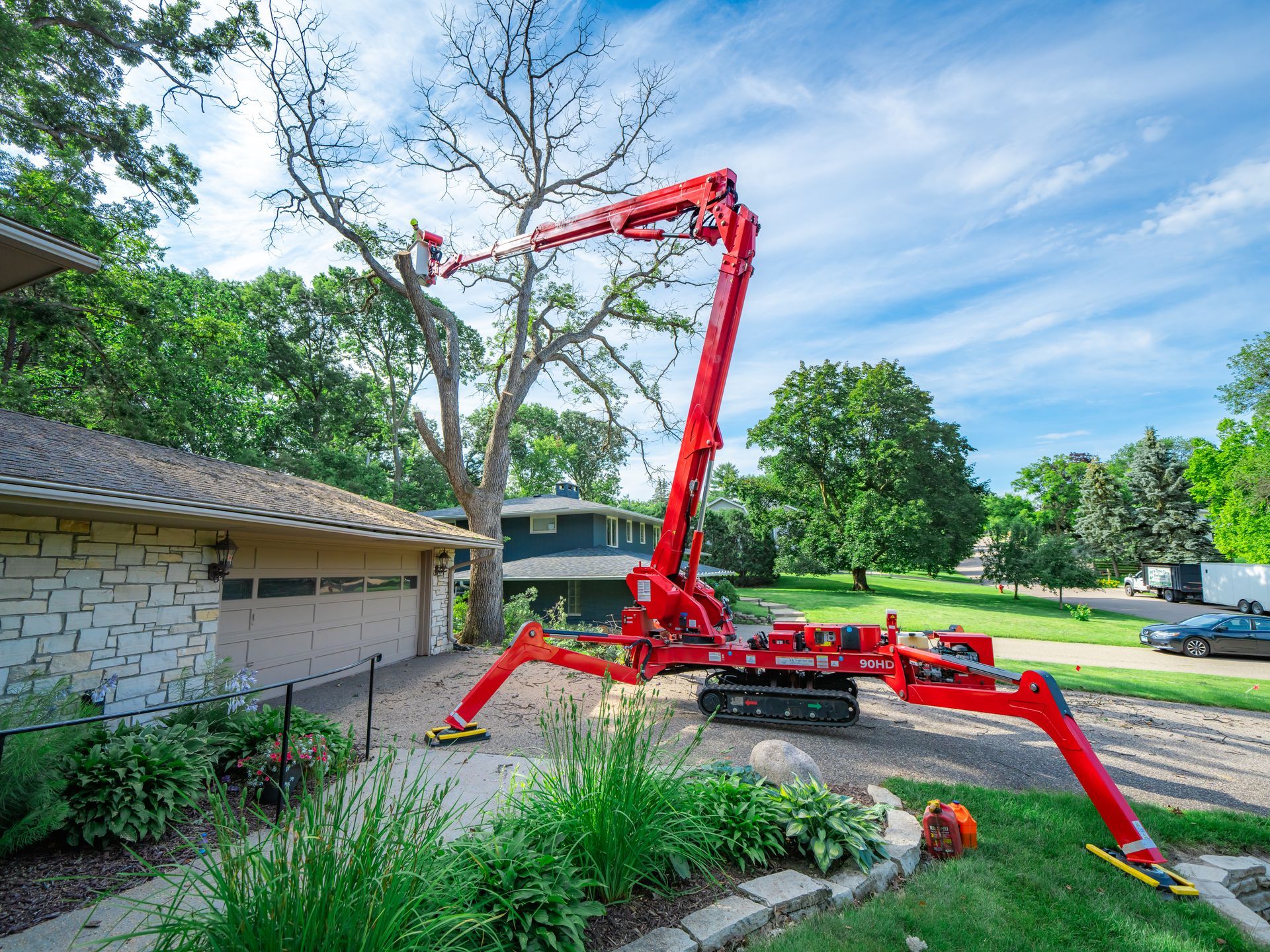 A red crane is cutting a tree in front of a house.
