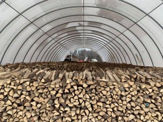 A large pile of logs is sitting inside of a greenhouse.