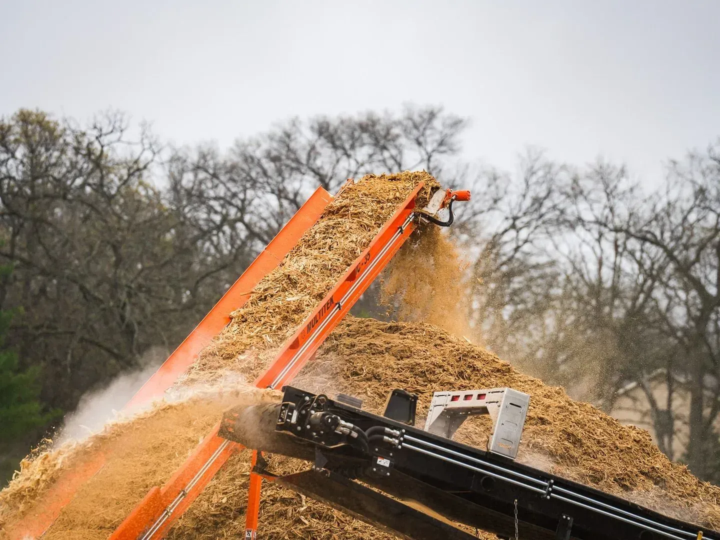A conveyor belt is carrying a pile of wood chips.