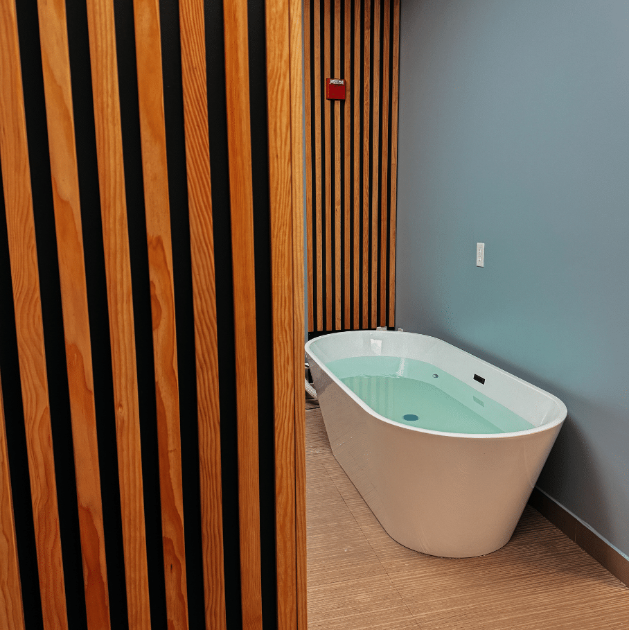 Modern spa room with a white oval soaking tub beside a wood slat wall and blue walls