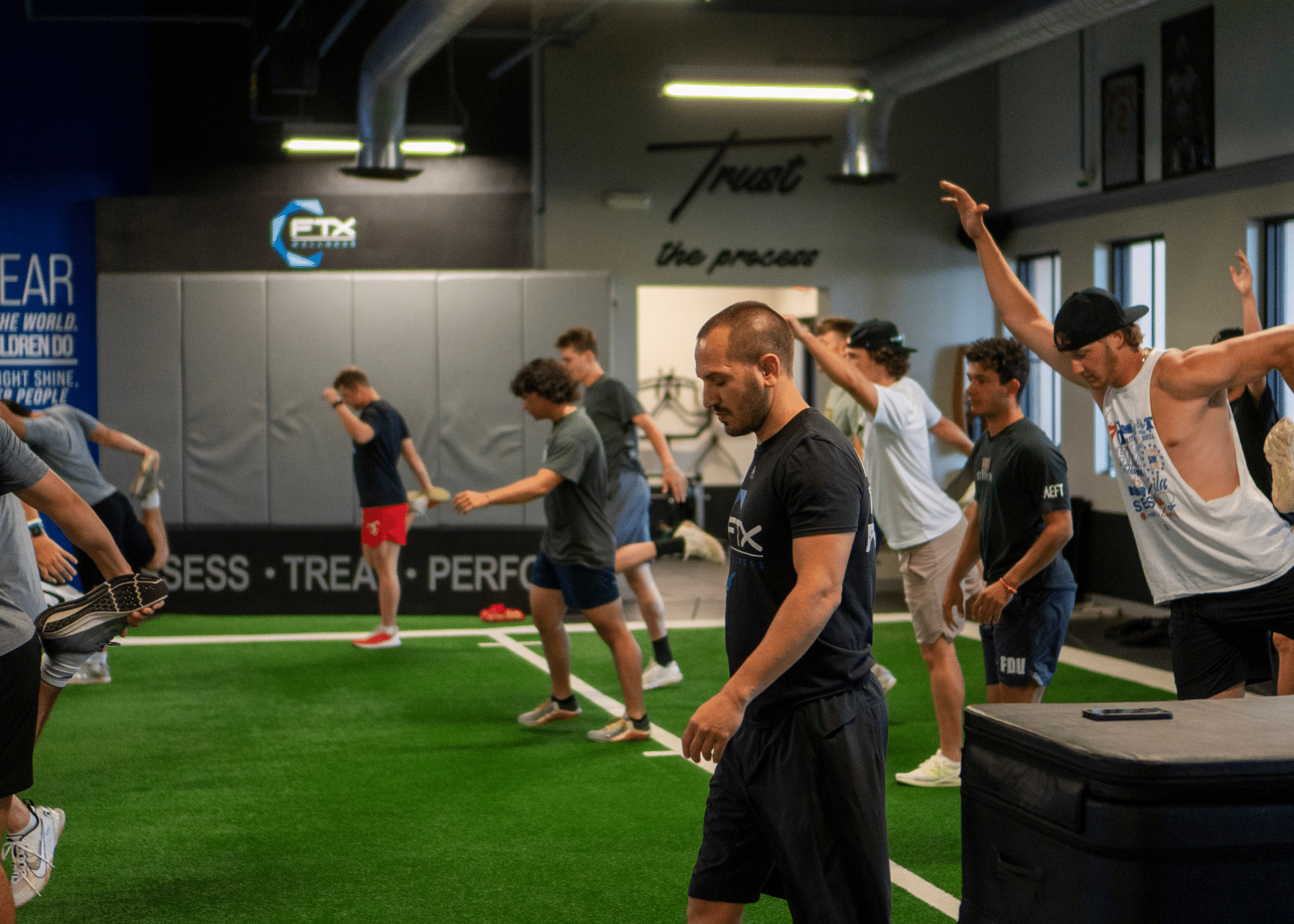 People exercising in FTX Performance in Boca Raton, FL on green turf, stretching and bending near workout equipment and mats
