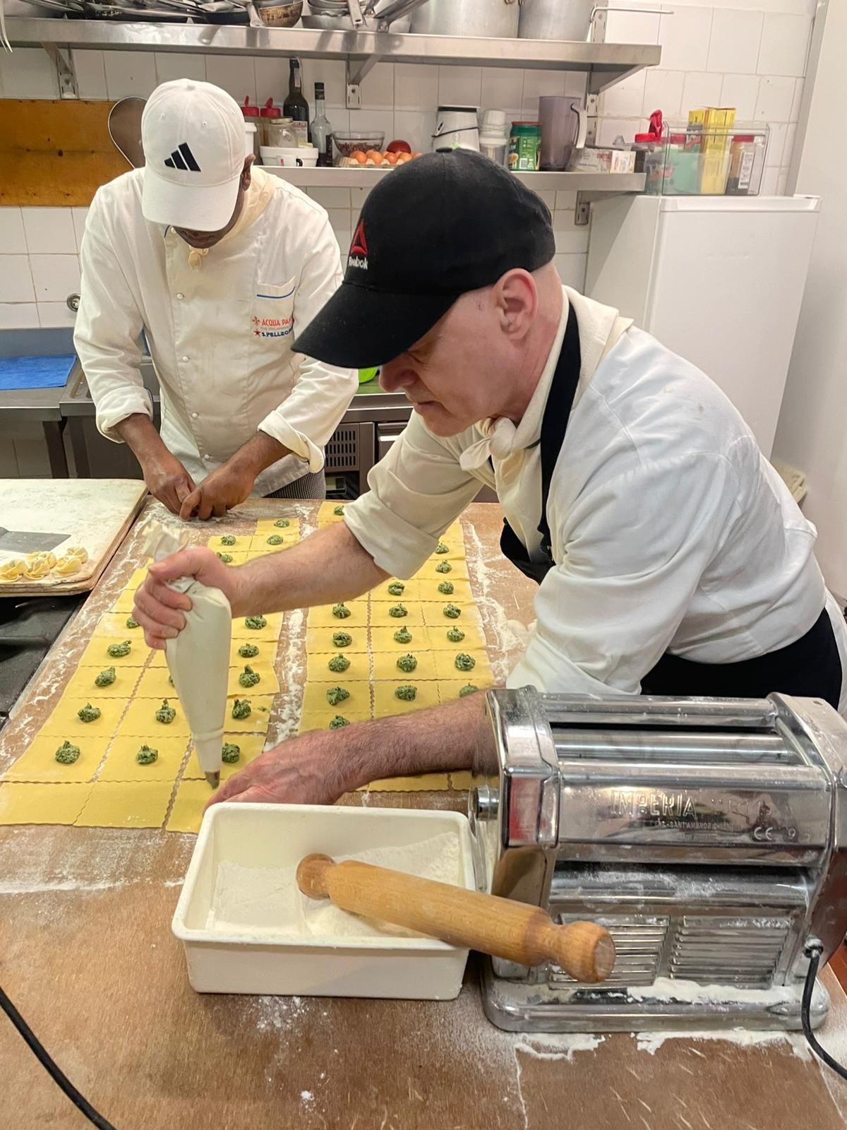 Due chef stendono la pasta su un bancone in una cucina professionale.