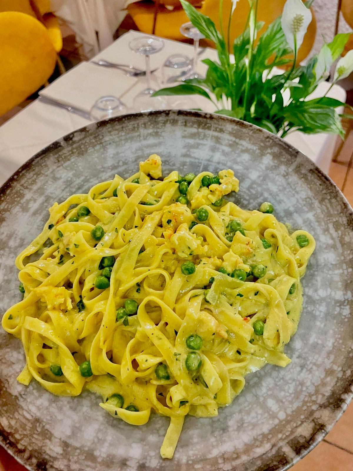 Pasta verde cremosa in una ciotola rustica su un tavolo, con una piccola pianta sullo sfondo.