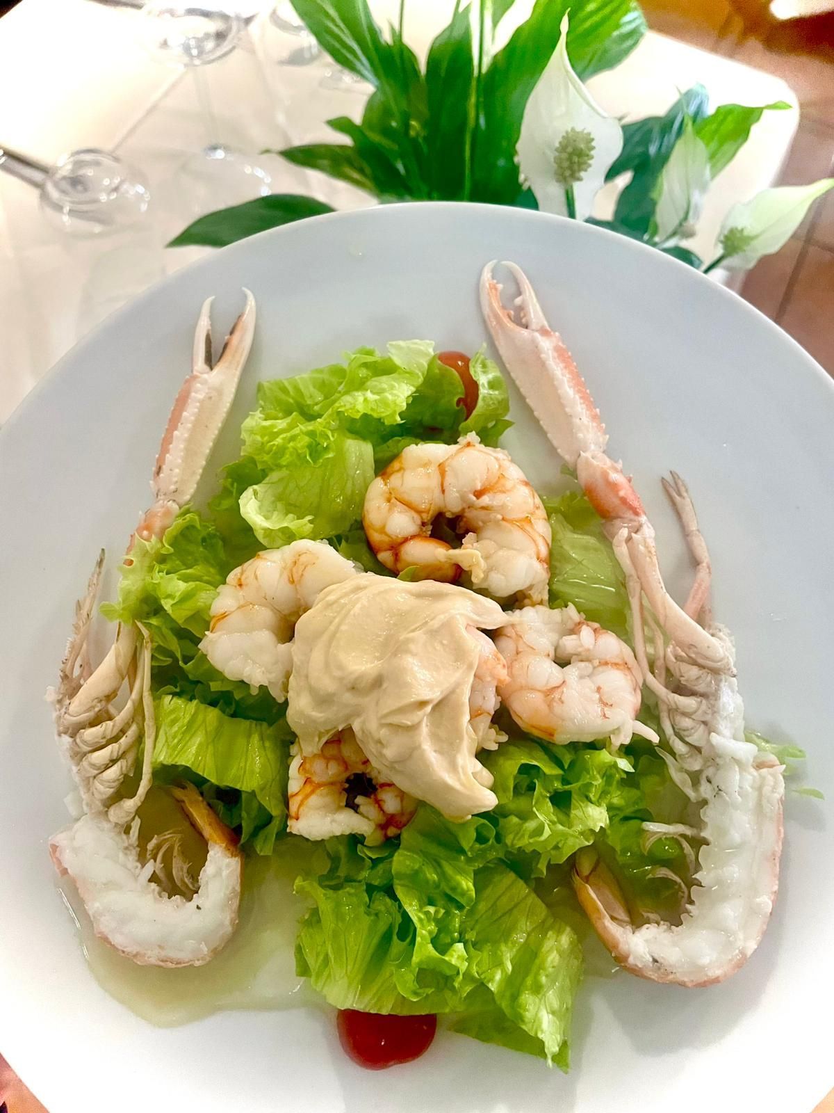 Insalata di frutti di mare su un piatto bianco con lattuga, gamberi e zampe di granchio disposti intorno al centro.