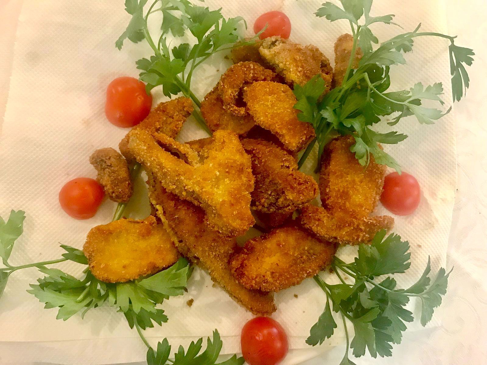 Piatto di fette di carne fritte dorate, guarnite con coriandolo e pomodorini, servite su una tovaglia bianca.