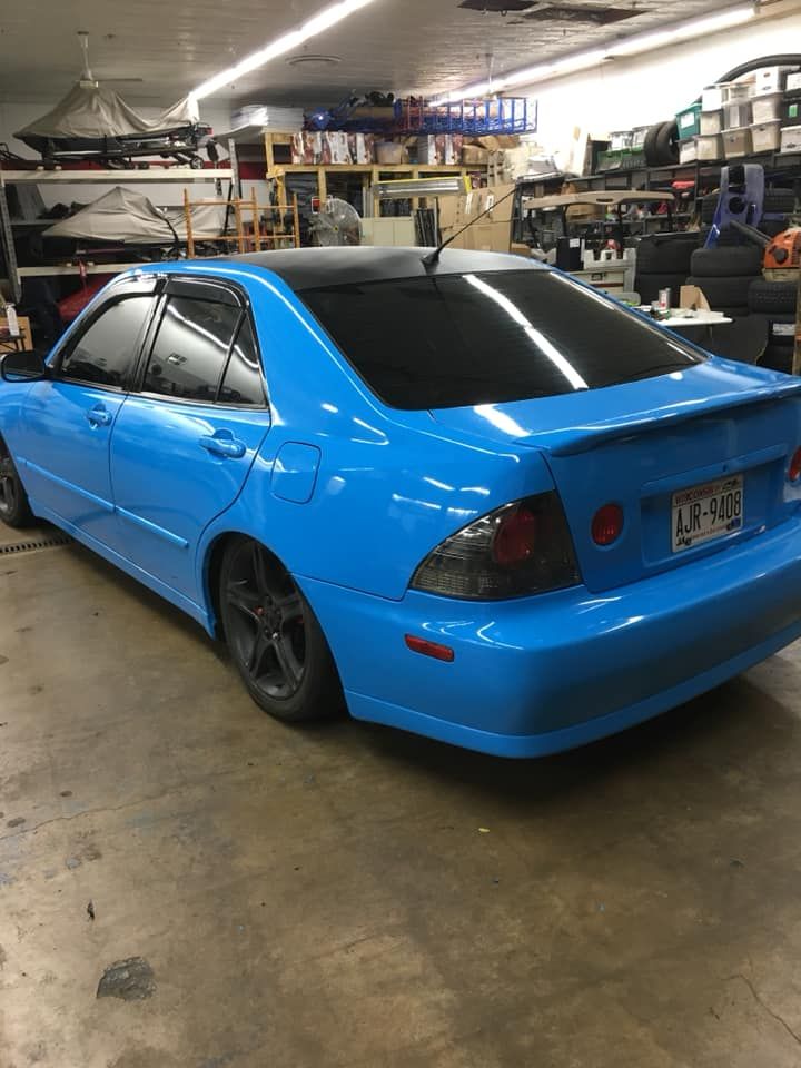 Bright blue sedan parked in a cluttered garage, rear three-quarter view, with dark tinted windows.