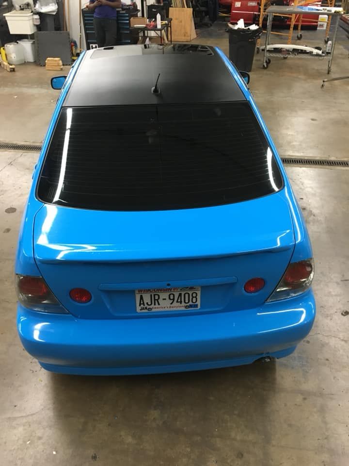 Blue sports coupe with black roof, parked inside a garage, viewed from the rear.