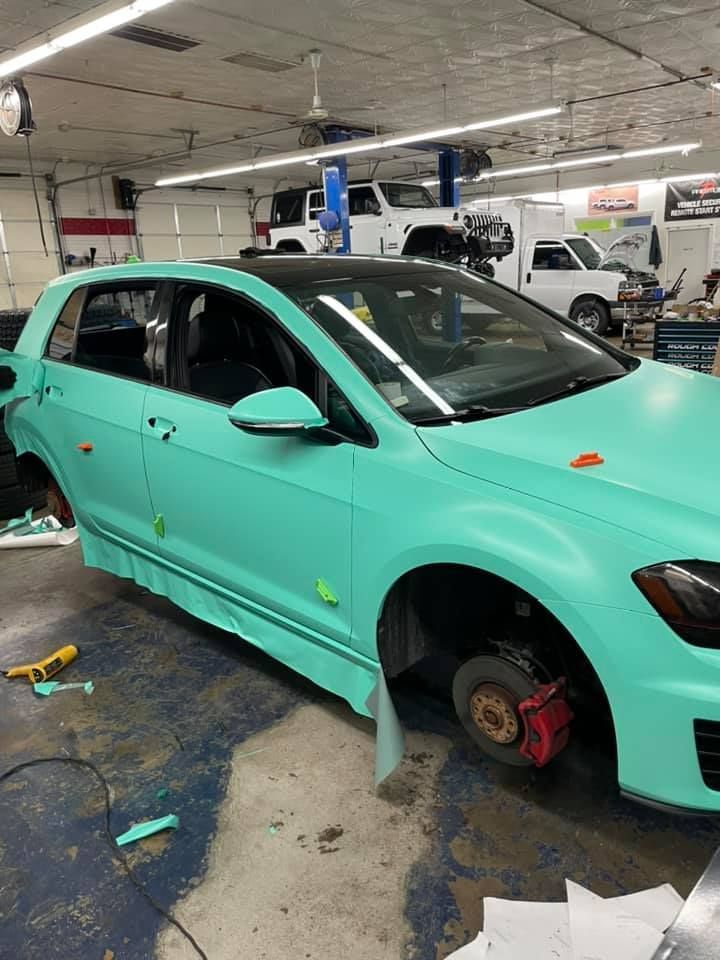 Mint green car in an auto repair shop with wheels removed and red brake rotor visible