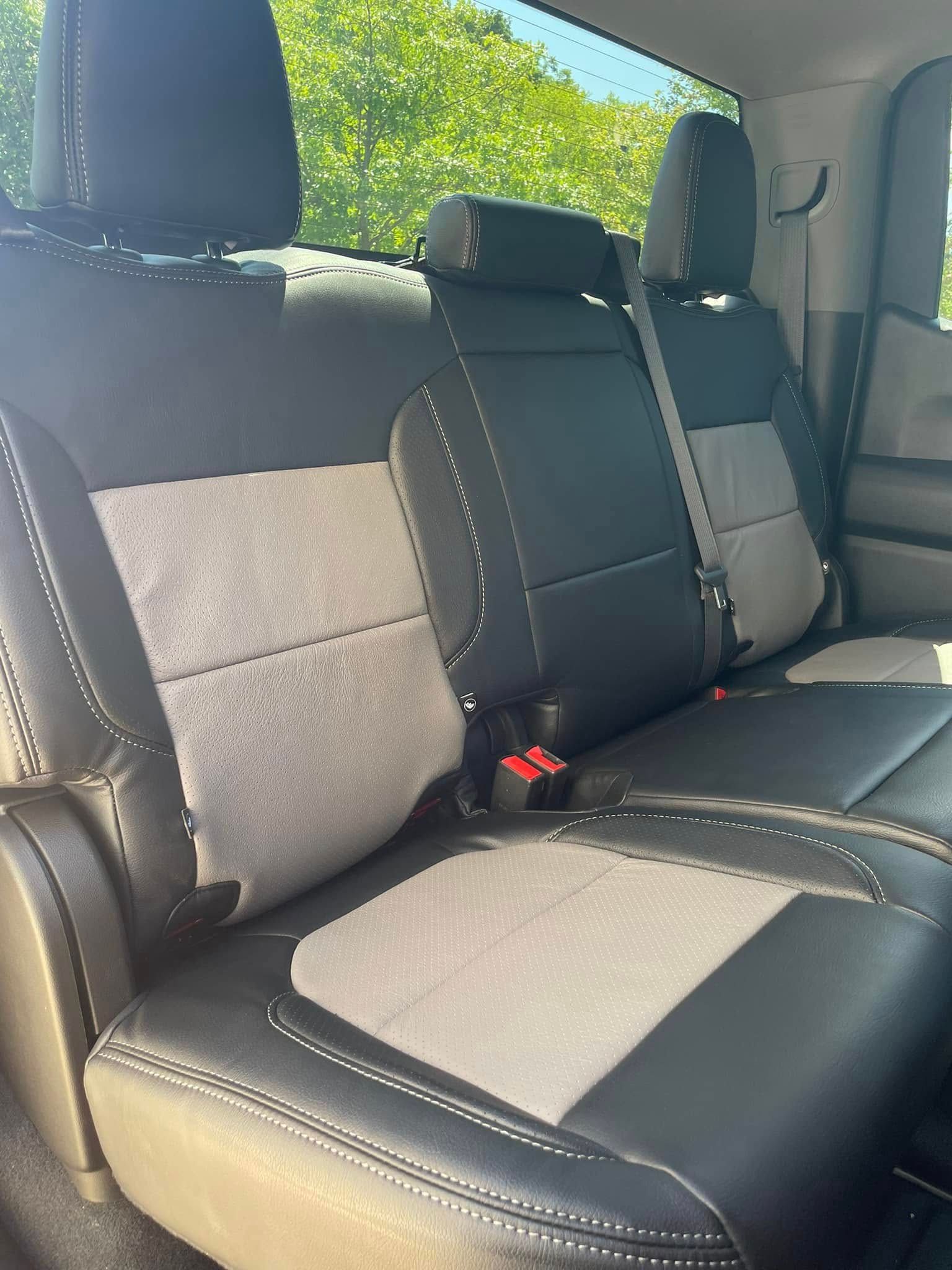 Rear seats of a car with black and gray upholstery and a center armrest, seen in daylight