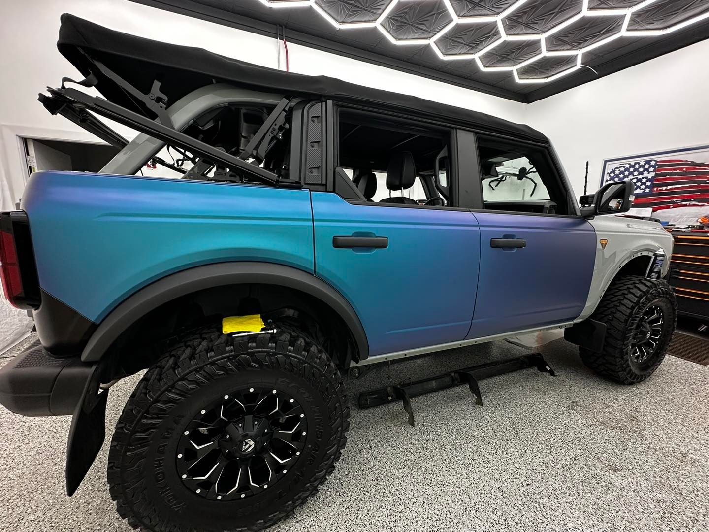 Blue and purple lifted off-road SUV with black wheels displayed indoors on a showroom floor