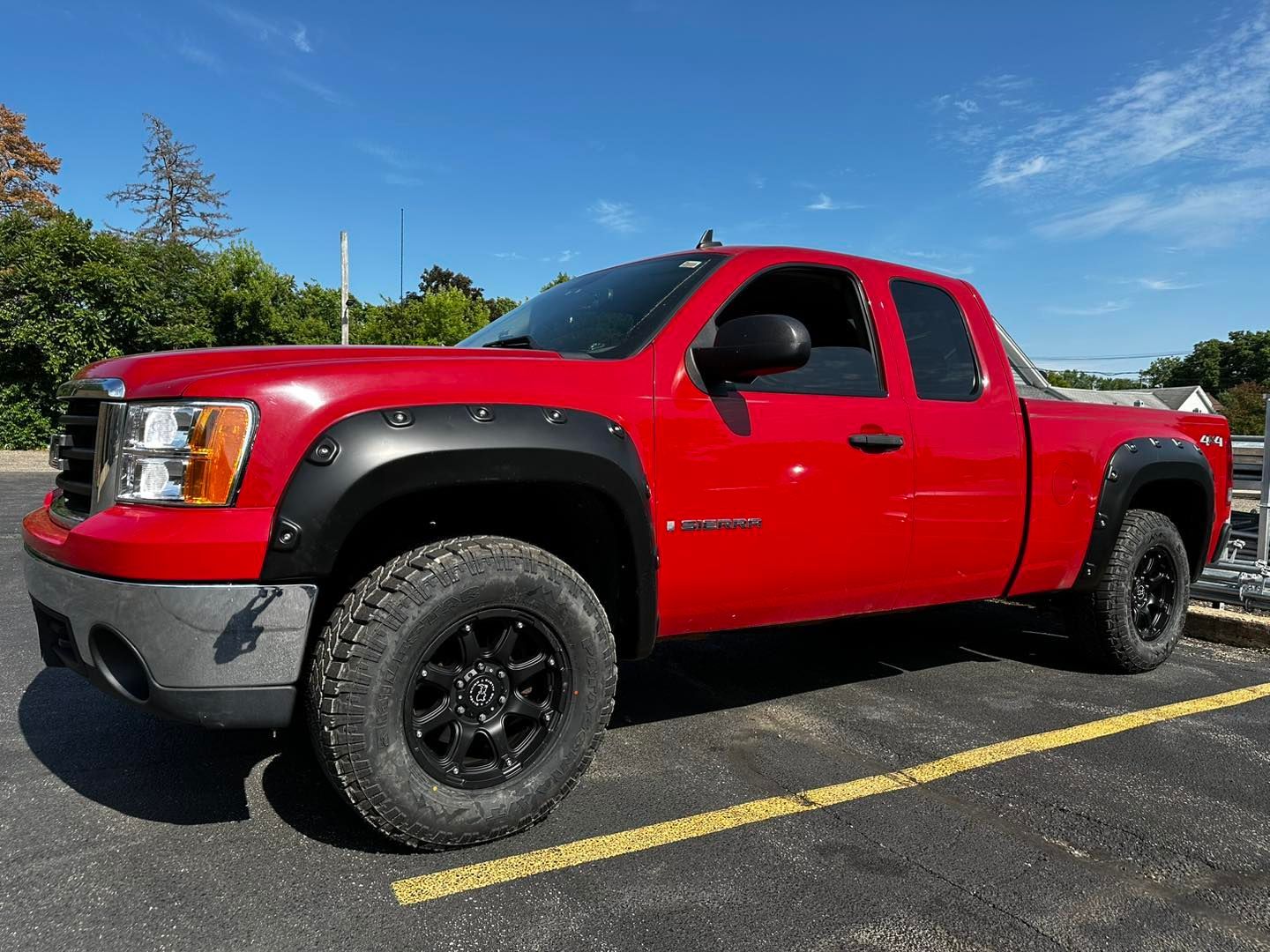 Red extended-cab pickup truck parked in a lot on a sunny day, side view.