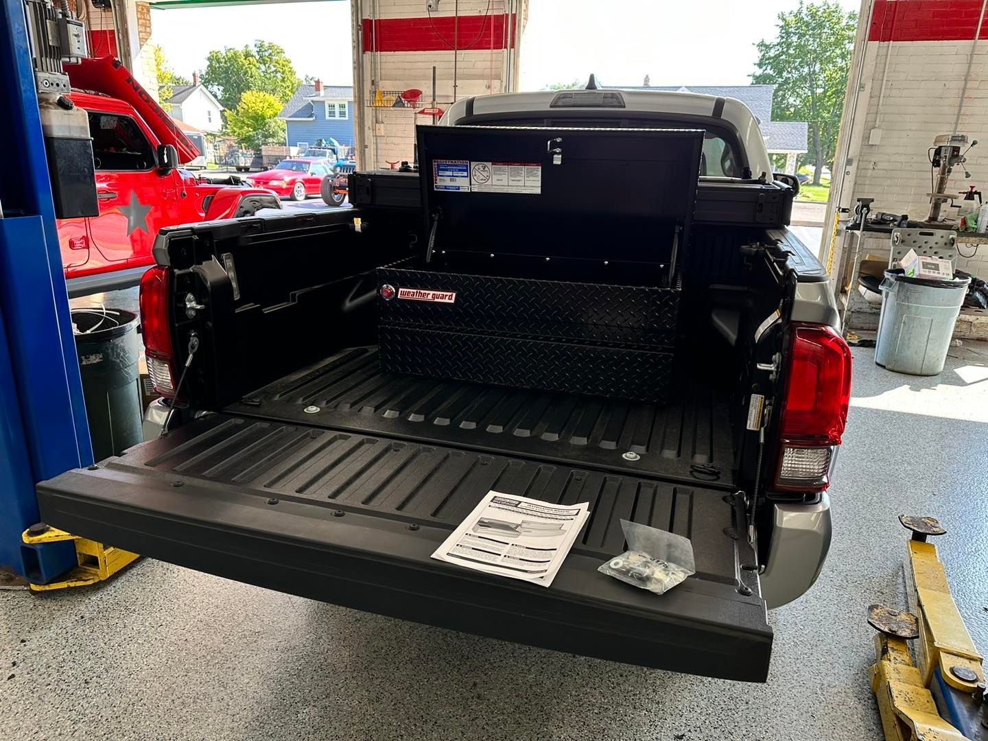 Black pickup truck tailgate open in a garage, showing a bed liner and protective cover.