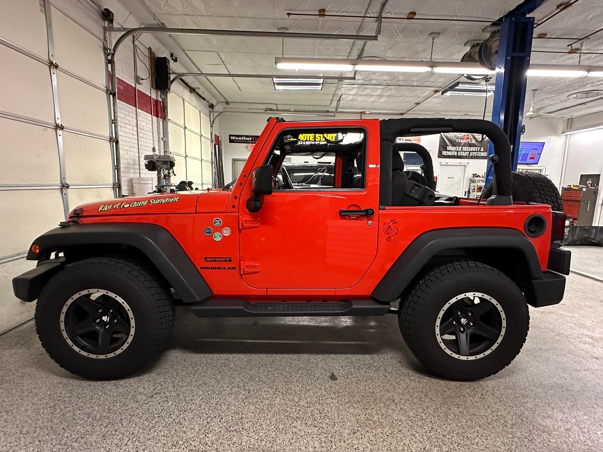 Red Jeep Wrangler parked in a garage, side view with black wheels and hardtop.