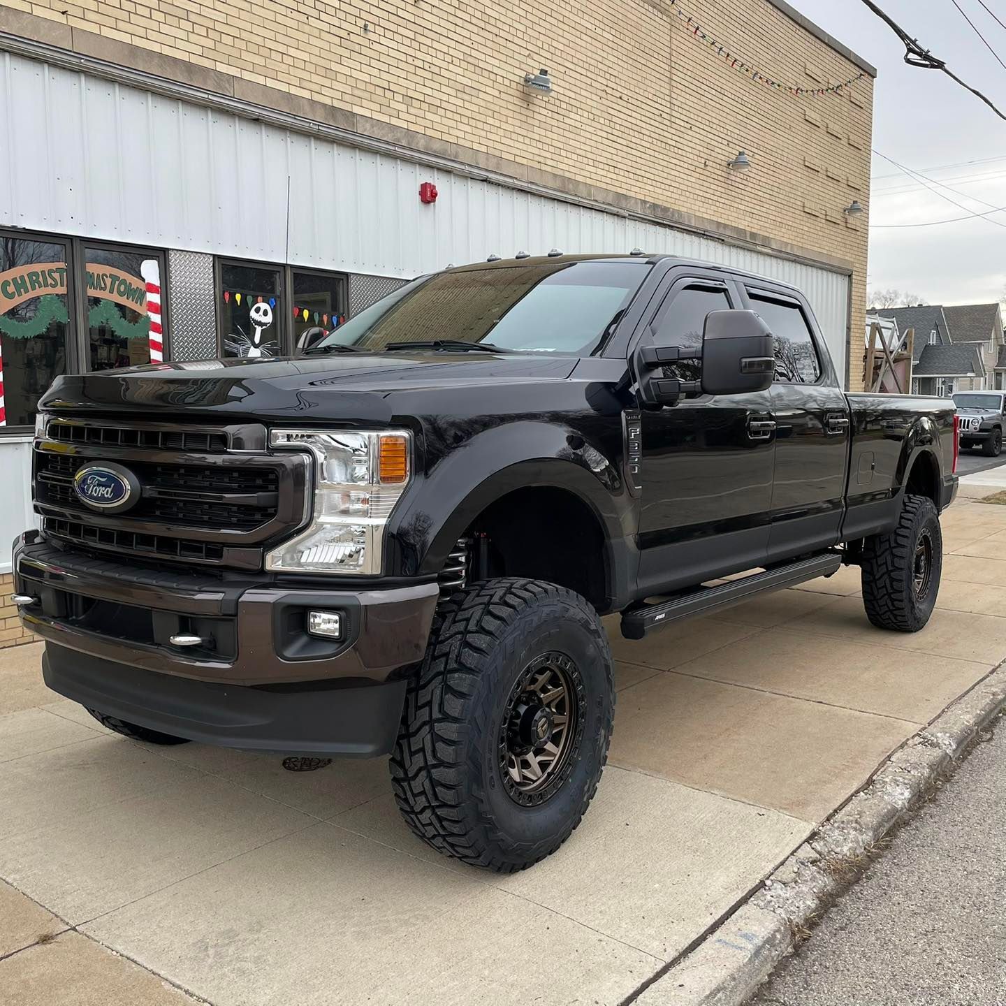 Black lifted Ford pickup truck parked outside a storefront on a sidewalk.