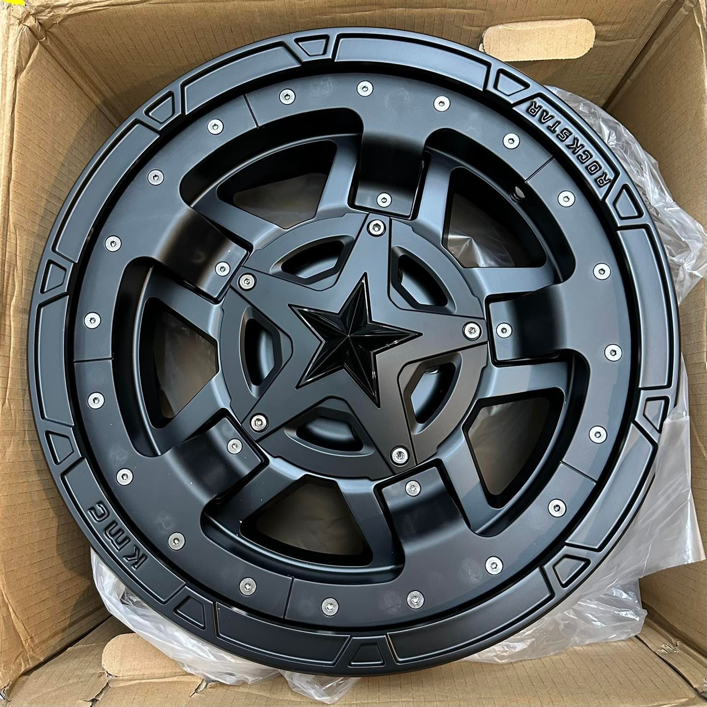 Black off-road wheel rim with star center, packed in a cardboard box