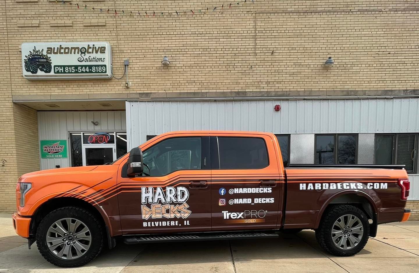 Orange pickup truck parked outside a beige building with a sign above the entrance.