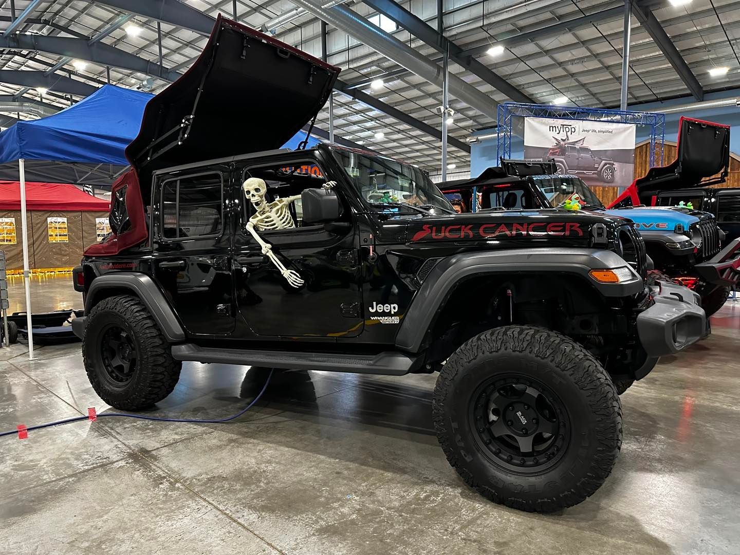 Black off-road Jeep with open hood in an indoor auto show hall
