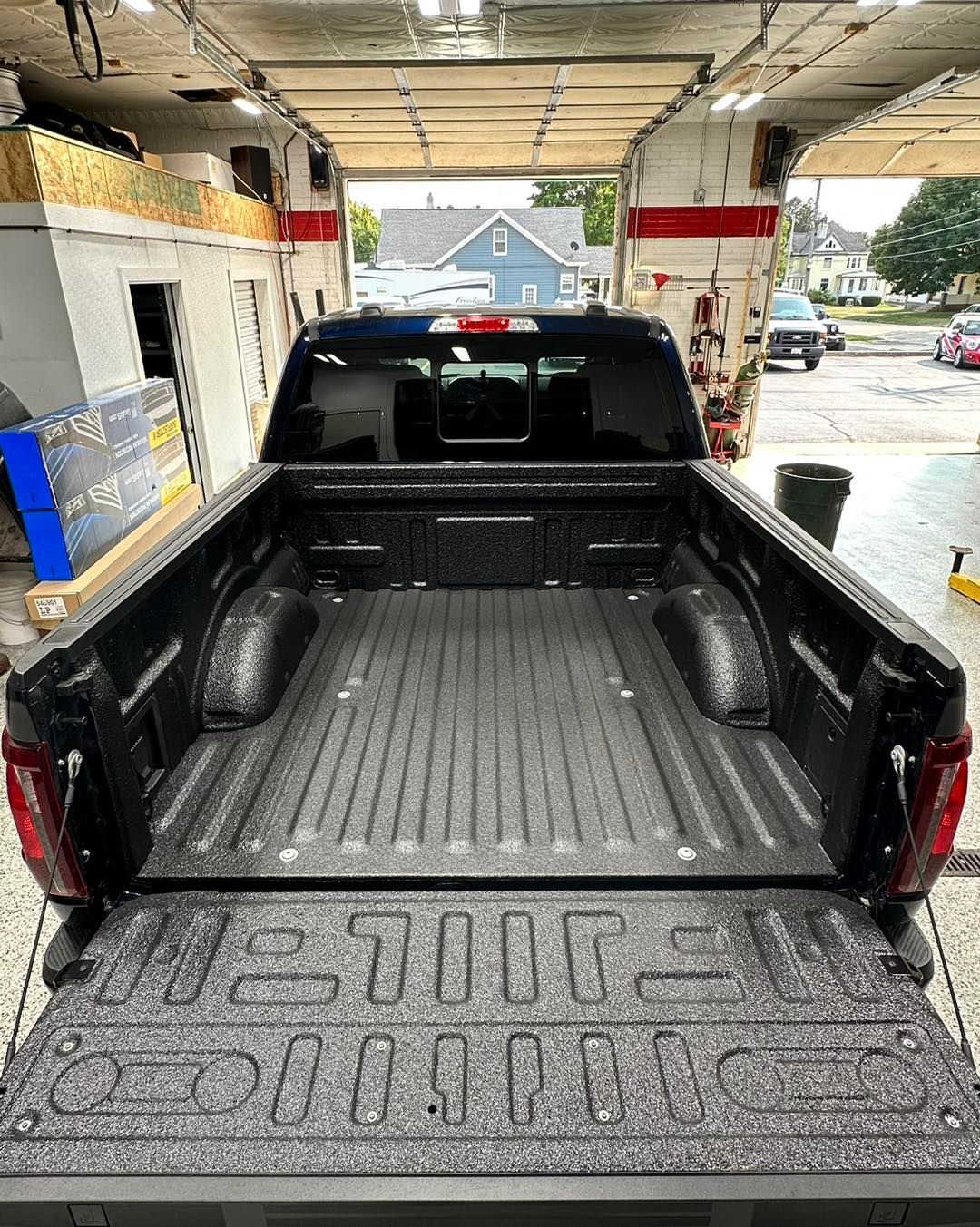 Black pickup truck parked under a covered car wash, bed liner visible, wet pavement outside.