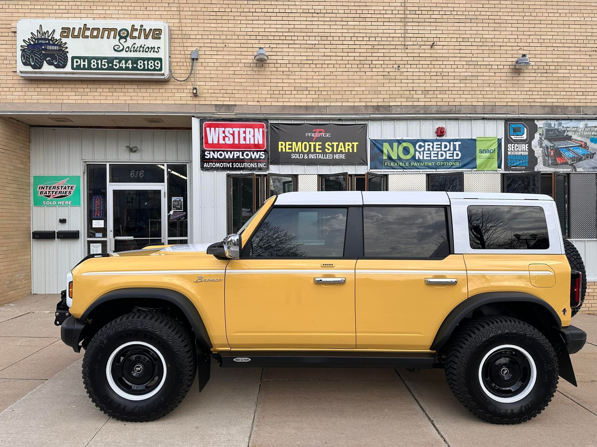 Yellow off-road SUV parked outside a storefront with signage on a brick building.