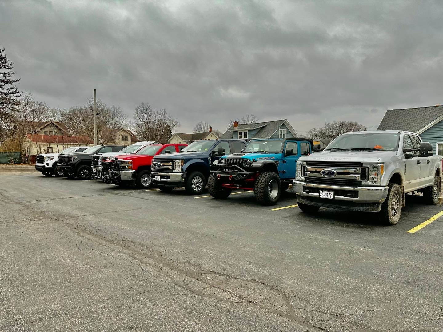 Line of parked pickup trucks in a lot under a cloudy sky