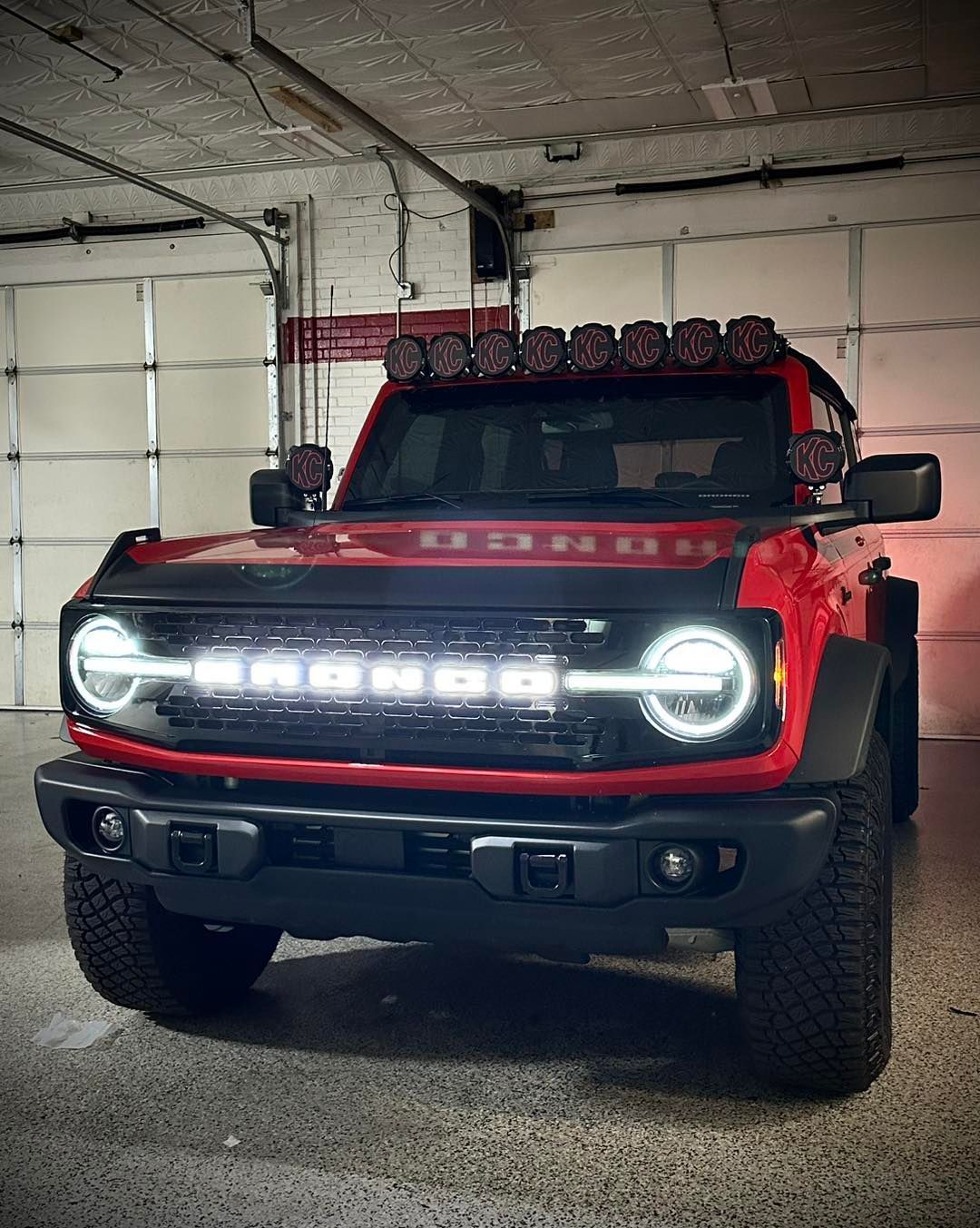 Red off-road truck with bright LED lights parked indoors in a garage.