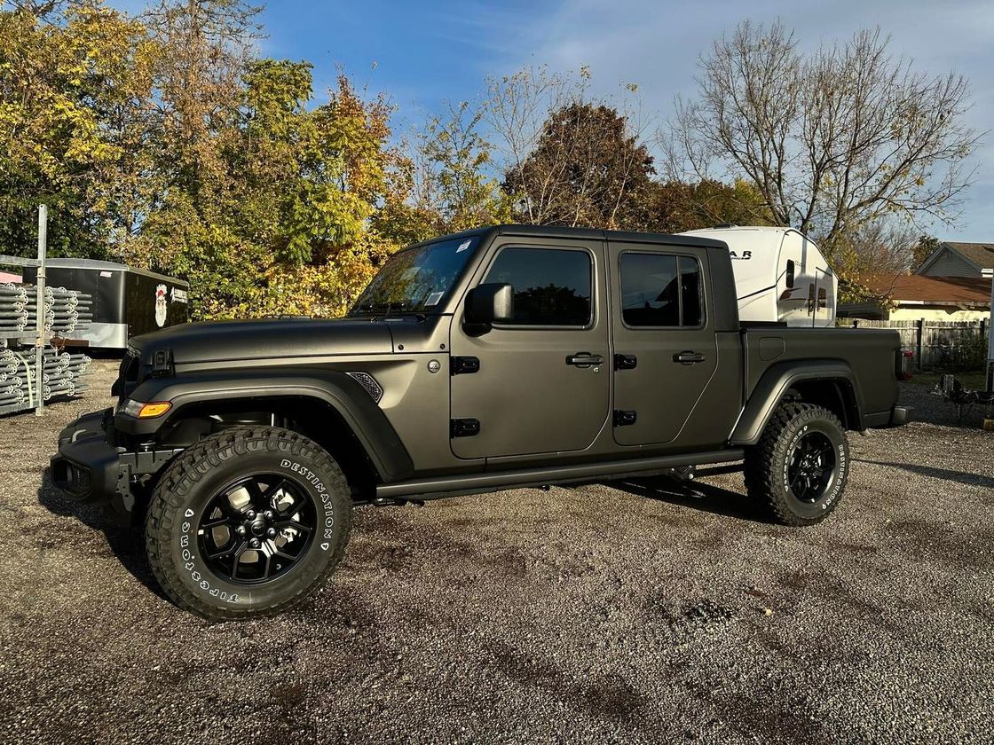 Olive-green lifted pickup truck parked on gravel under autumn trees
