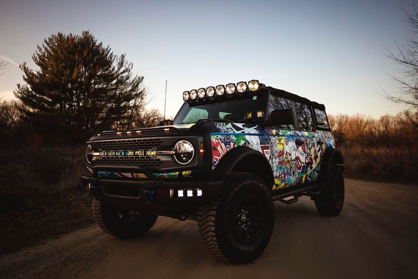 Custom off-road SUV with colorful wrap and roof lights on a road at sunset