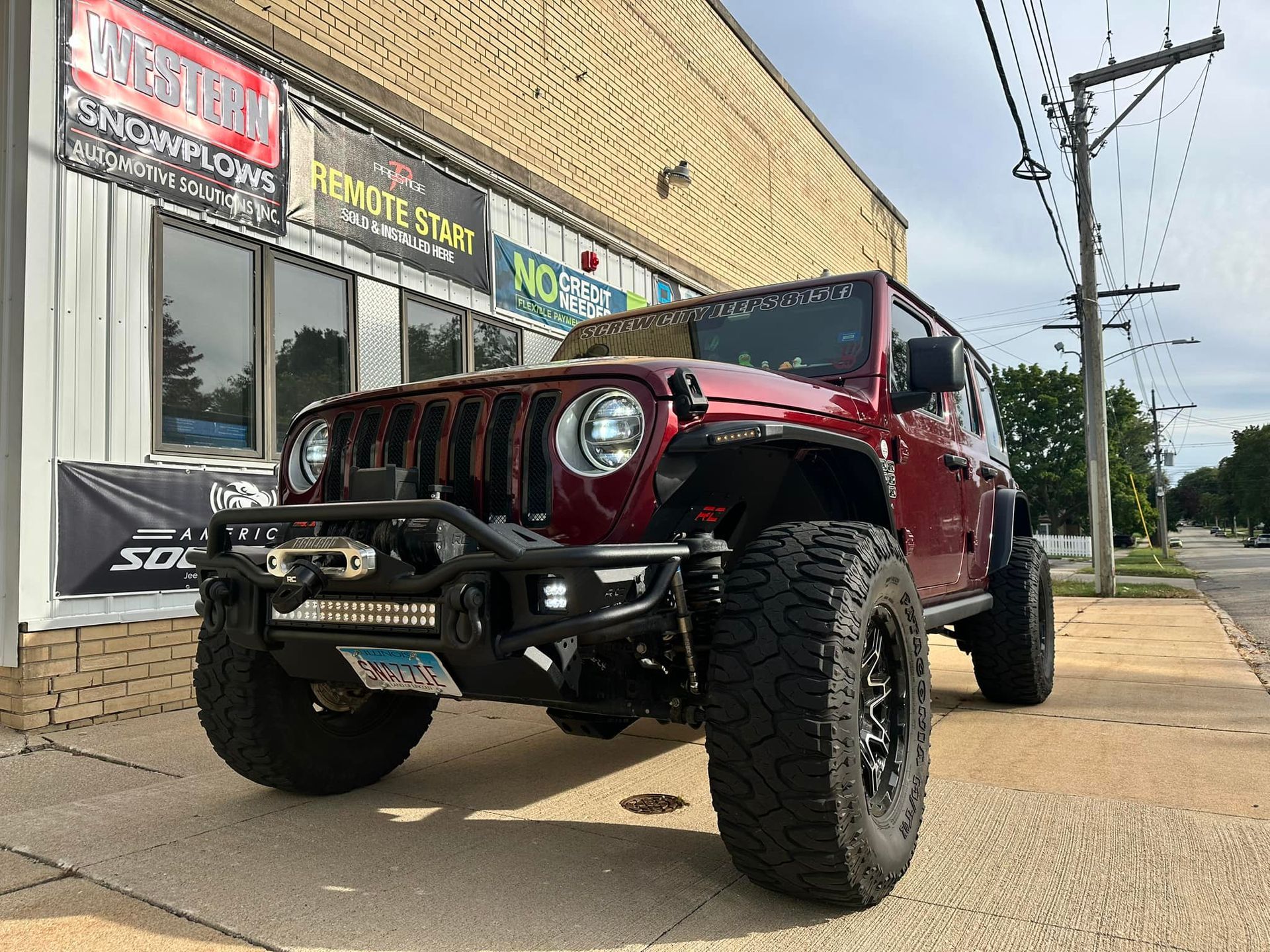 Red lifted Jeep Wrangler parked outside a storefront on a sidewalk.