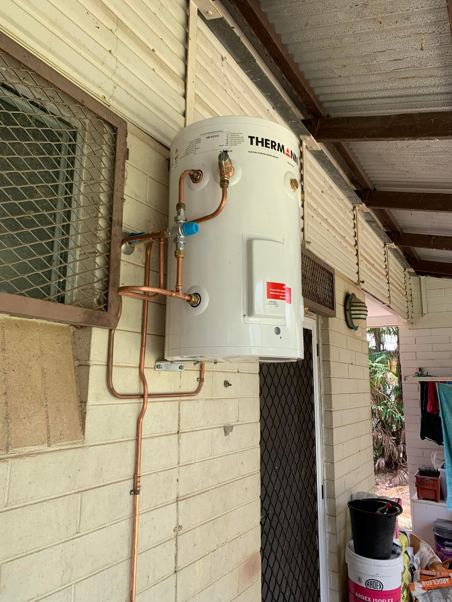 A White Water Heater with Copper Pipes Mounted on A Beige Wall — 2 Foote Plumbing & Gas in Darwin, NT