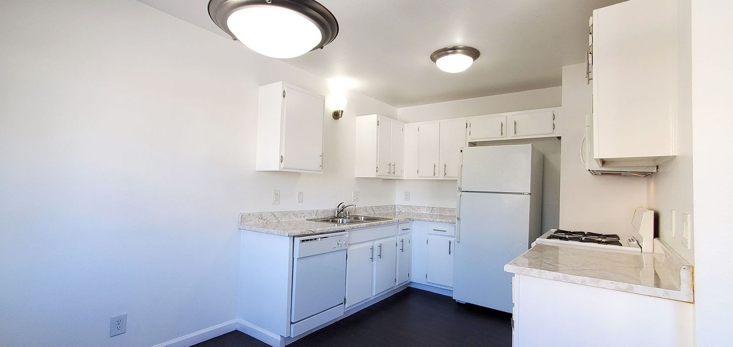 A kitchen with white cabinets , a refrigerator , a stove , and a sink.