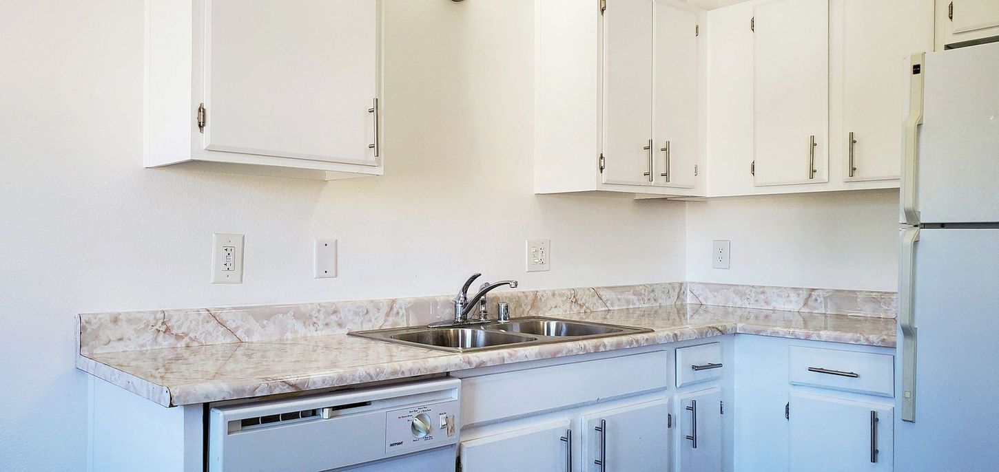 A kitchen with white cabinets , granite counter tops , a sink and a refrigerator.